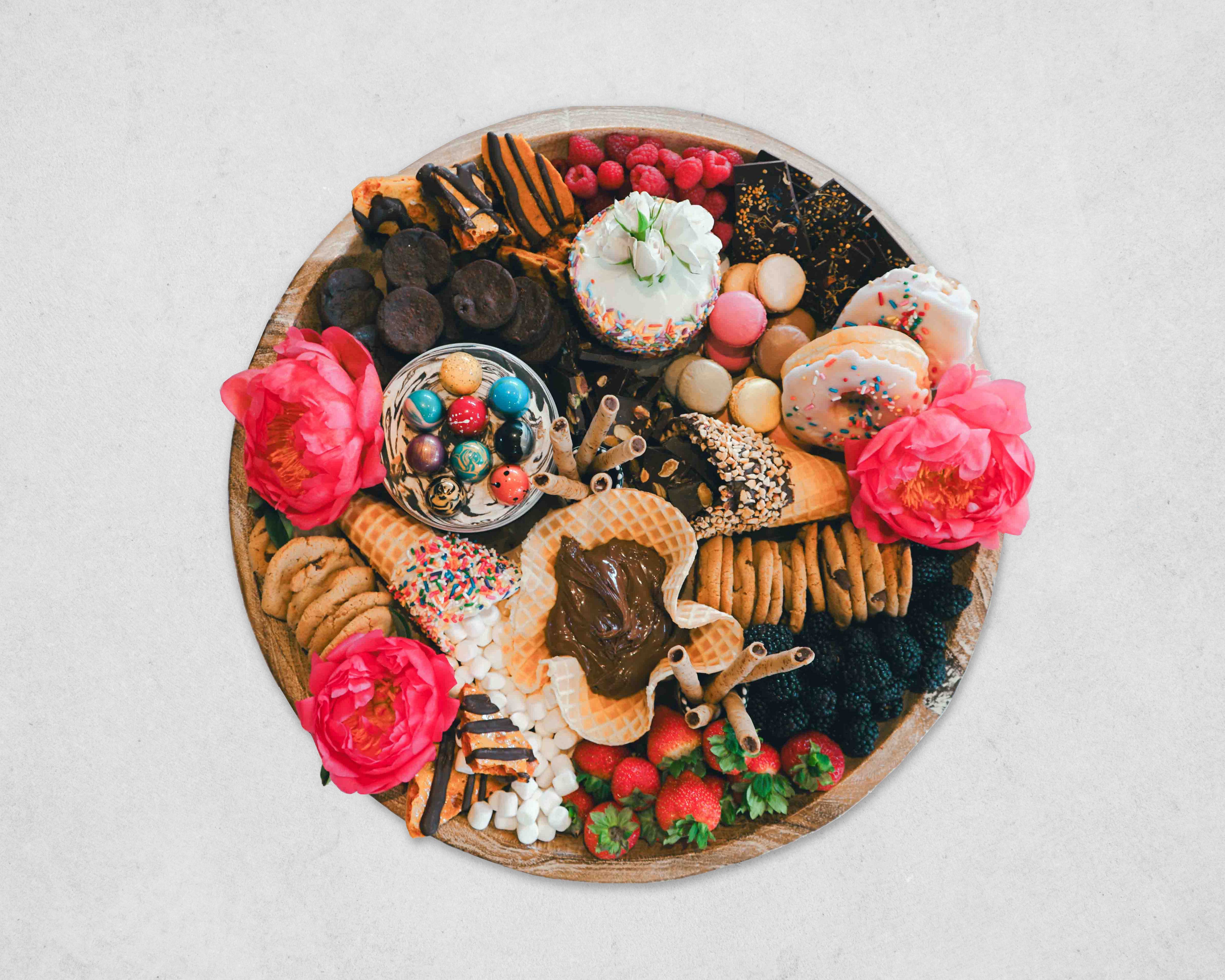 Assorted cookies, candies, and flowers on a wooden board with a white background
