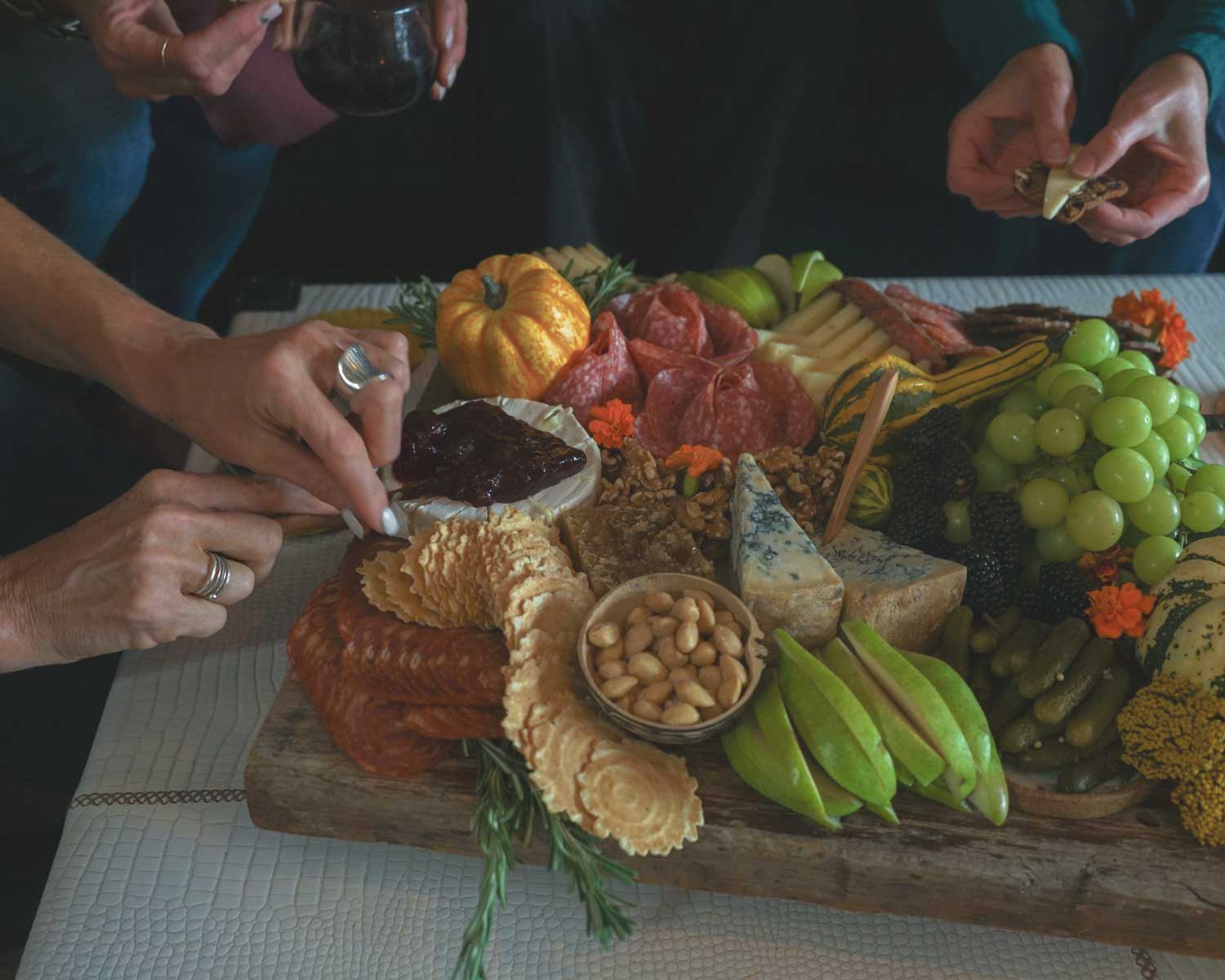 People enjoying a charcuterie board with various foods on a table.