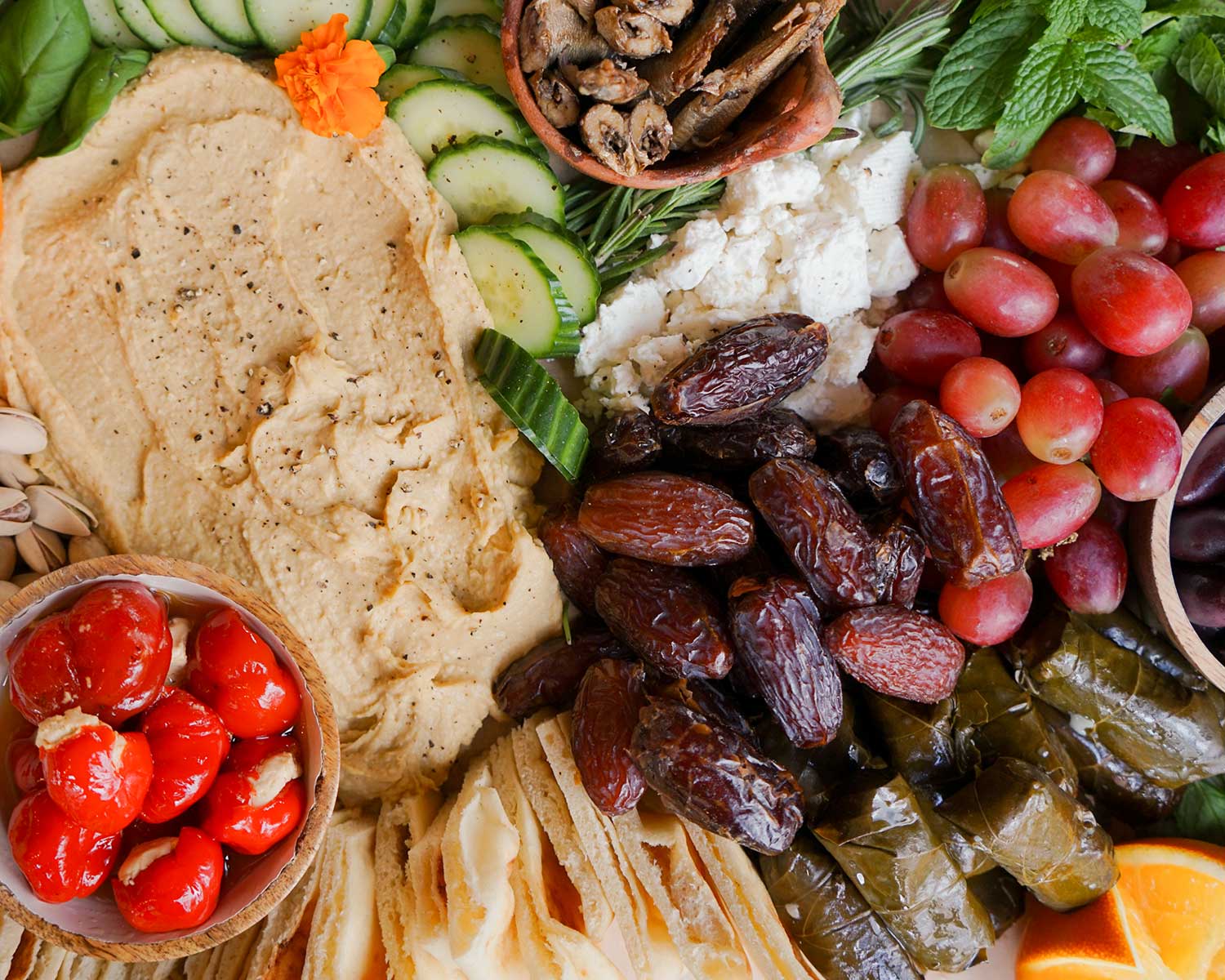 Platter of hummus, olives, grapes, and other snacks on a wooden board.