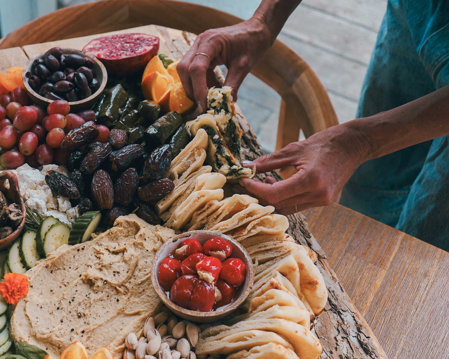 Person arranging food on a charcuterie board with various fruits, cheeses, and meats.