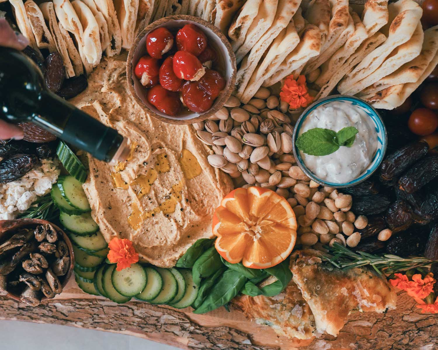 Gourmet platter with hummus, vegetables, nuts, and dips on a wooden board.