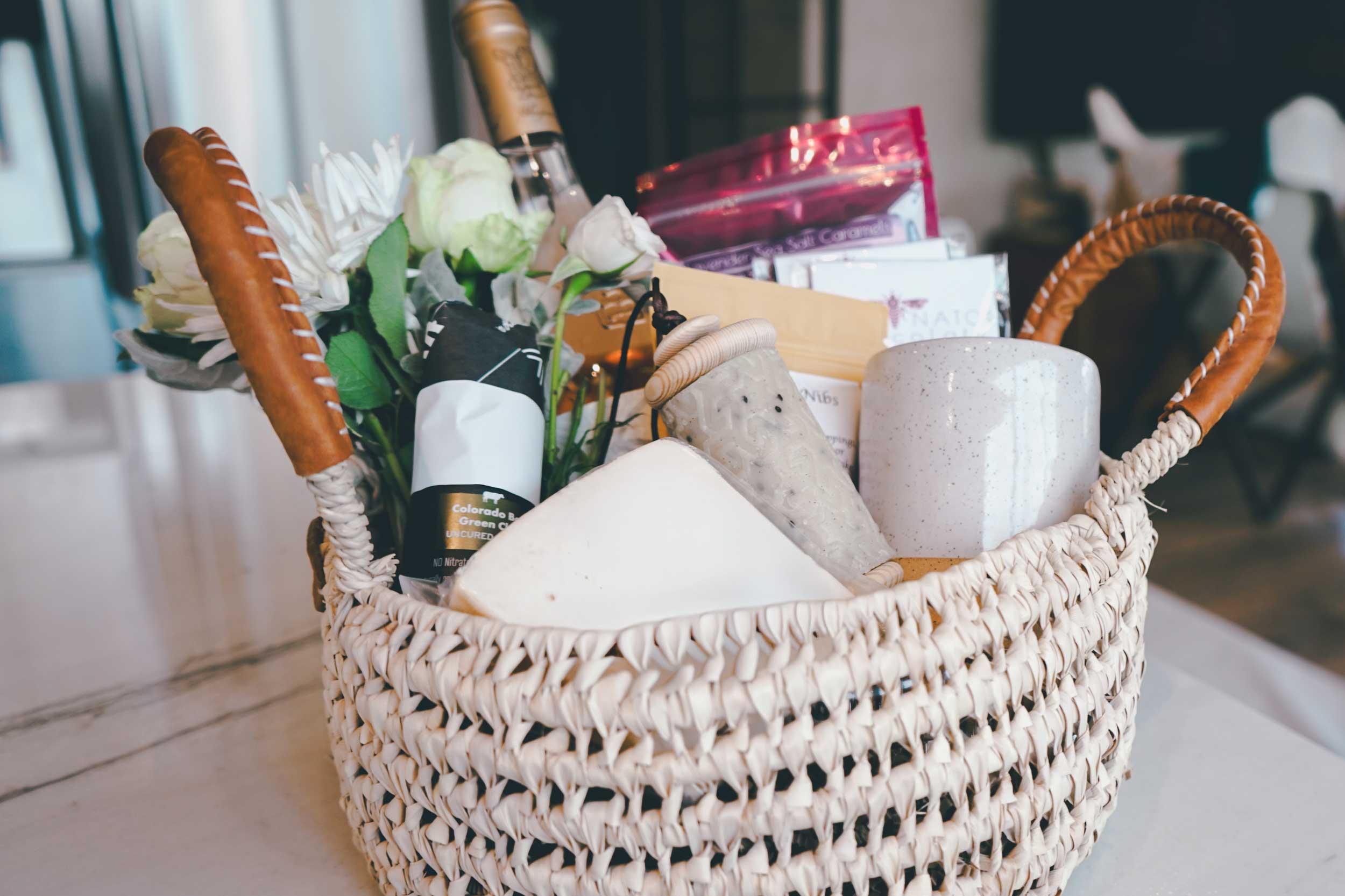 Woven basket with wine, flowers, and other items on a table
