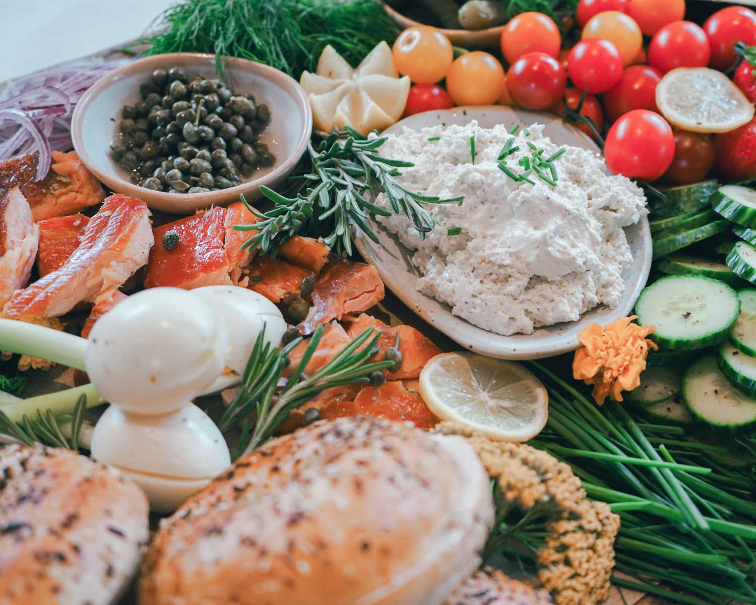 Assorted food items including fish, vegetables, and herbs on a wooden board.