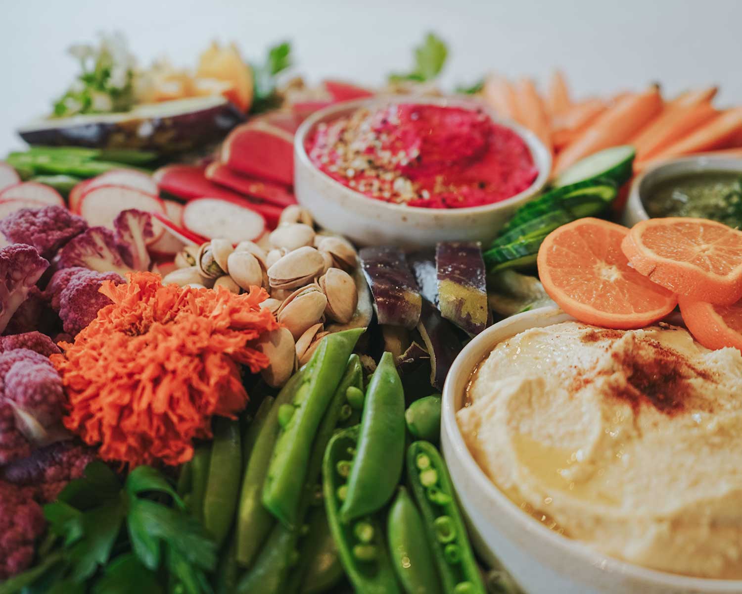 Assorted platter with hummus, vegetables, and fruits on a white background