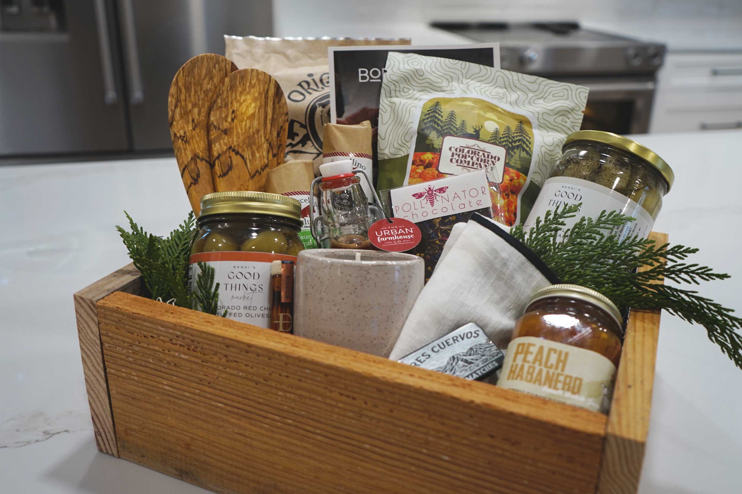 Gift basket with jars, a wooden spatula, and other items on a kitchen counter.