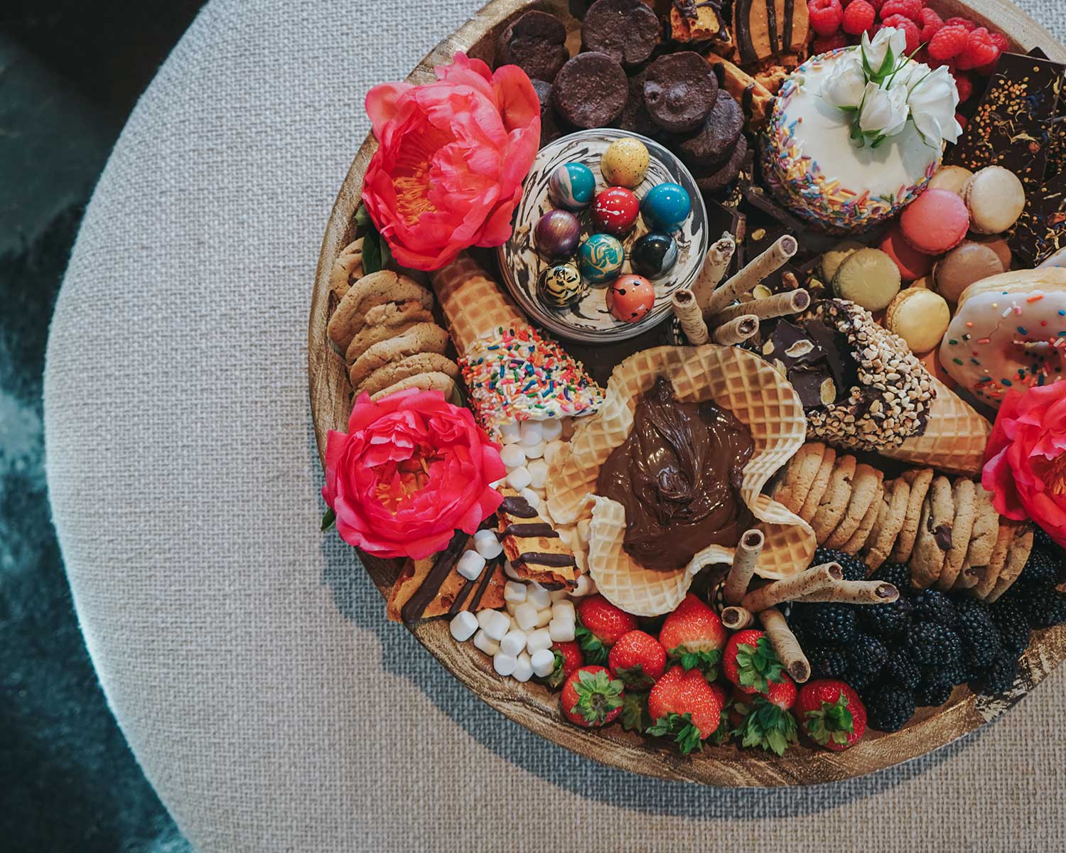 Assorted desserts including cookies, pastries, and fruits on a wooden board with flowers.